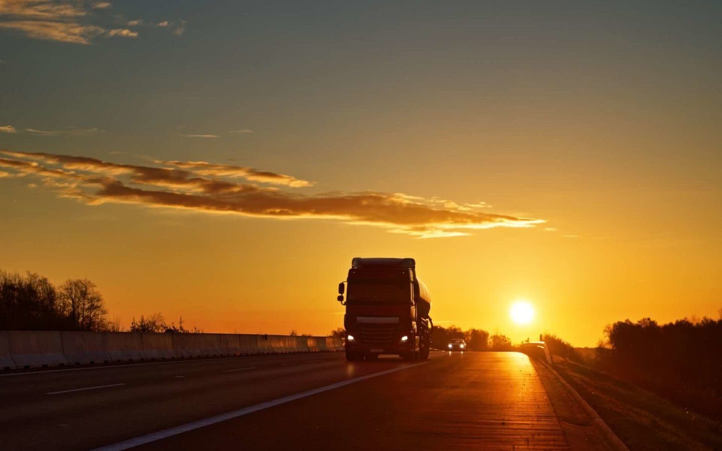 Lastbil som kör på motorväg i solnedgång med en gyllene himmel.
